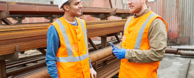 Two workers in uniform chat during break outside of modern metalworking plant