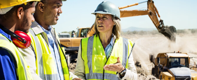 Architects and worker discussing over blueprint at quarry against clear sky