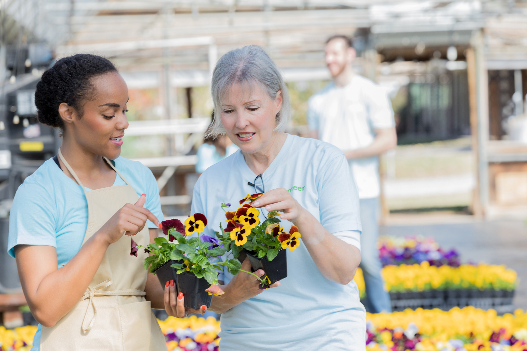 Two female plant nursery workers discuss flowering plant