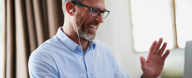 Businessman waves while using laptop to work from home